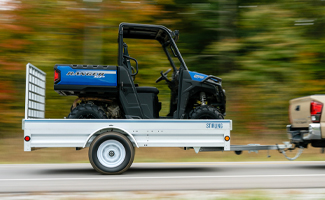 An off-road recreational vehicle being hauled down a tree-lined road in a Stirling trailer.
